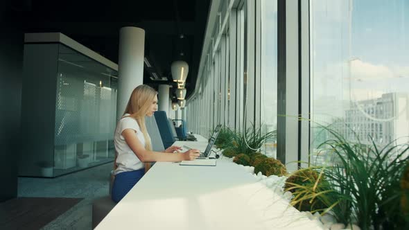 Businesswoman Working with Laptop in New Office. Side View of Woman Sitting at Table Alongside