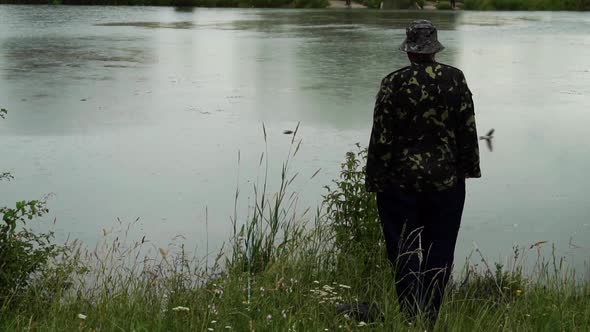 Fisherman Stands Near the Lake in the Rain Amid Flying Birds