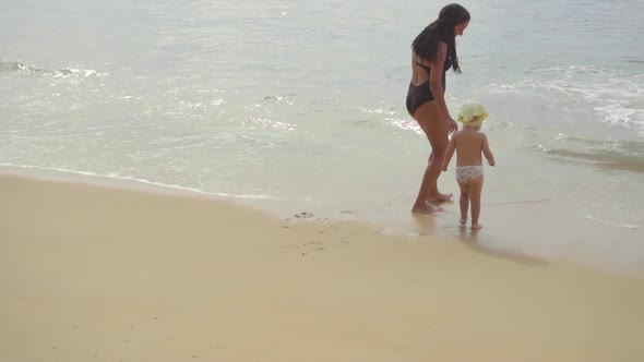 Mom with a Two-year-old Daughter Walking Along the Sandy Beach