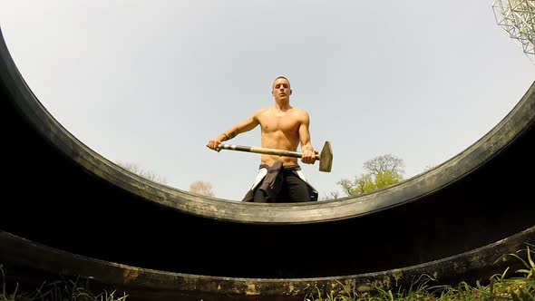 Close Up Of A Muscular Man Hitting Tire With A Hammer 1