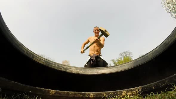 Close Up Of A Muscular Man Hitting Tire With A Hammer 3