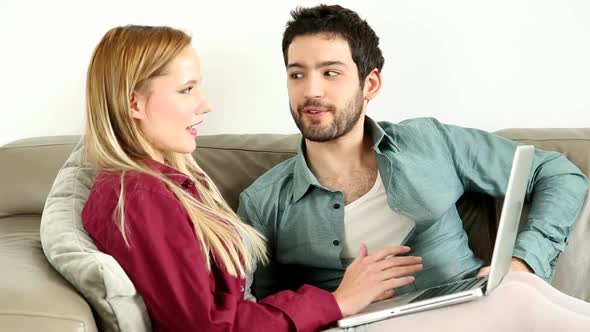 Young Couple Sitting On Couch On Laptop At Home 1