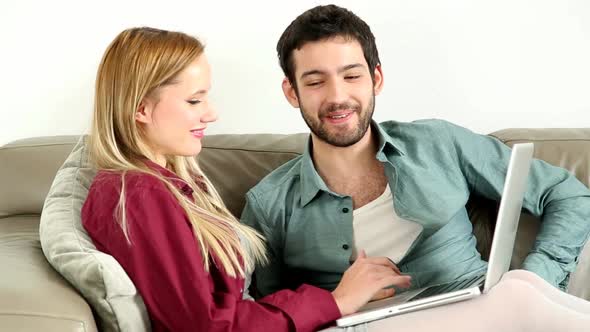 Young Couple Sitting On Couch On Laptop At Home 2