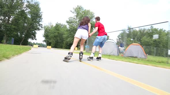 Young Woman And Man Rollerblading And Performing In Park On A Beautiful Warm Day, Doing Tricks