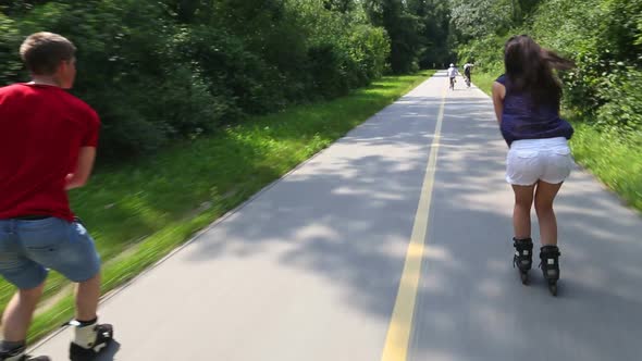 Young Woman And Man Rollerblading On A Beautiful Sunny Summer Day In Park, Holding Hands