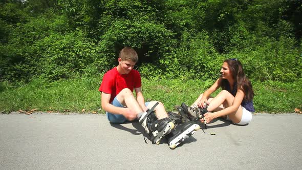 Young Woman And Man Sitting On Track, Putting Their Rollerblades On Their Feet. 4