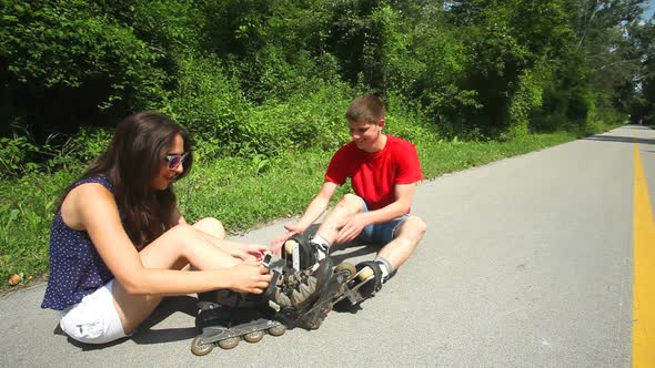 Young Woman And Man Sitting On Track, Putting Their Rollerblades On Their Feet. 6