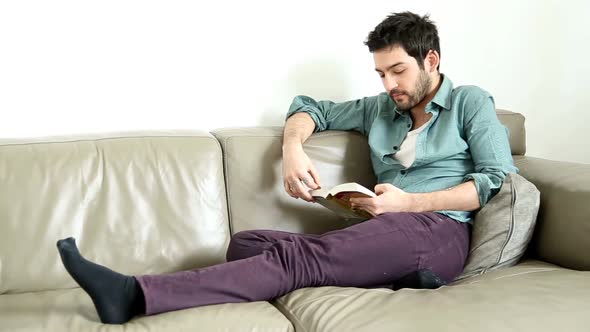 Cute Man Sitting On Couch Reading Book And Smiling alt