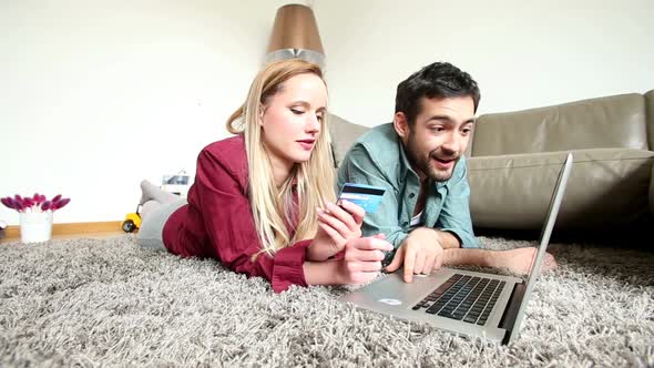 Man And Woman On Carpet In Living Room Doing Online Shopping