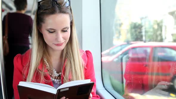 Blond Young Woman Riding Tram, Reading Book