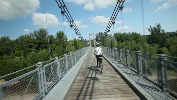 Slow Motion - Woman Cycling On Road Over Suspension Bridge