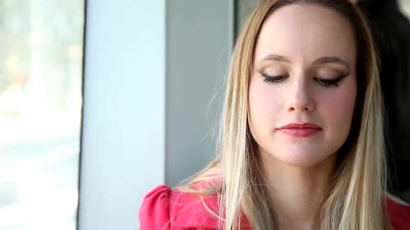 Young Blond Woman Riding Tram, Looking To The Camera And Talking On Phone alt
