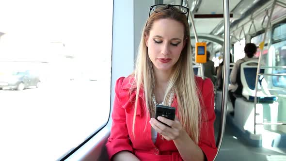 Young Blond Woman Riding Tram, Typing On Mobile, Phone, Cell, Smiling