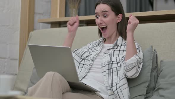 Ambitious Young Woman Celebrating Success on Laptop on Sofa