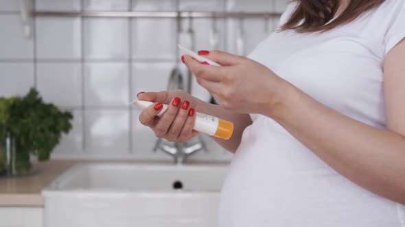 Pregnant Woman Hands with Smartphone Reading Label on a Bottle