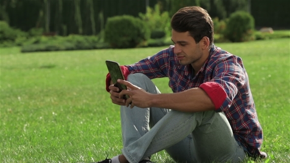 Male Sitting On The Grass Using a Tablet