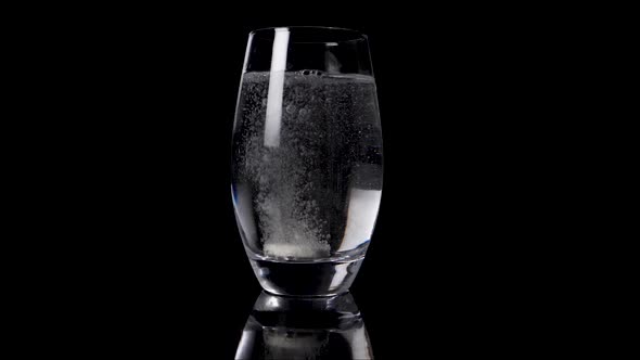 Slowmotion footage of falling vitamin pill tablet dissolving  in clean water in front of black backg