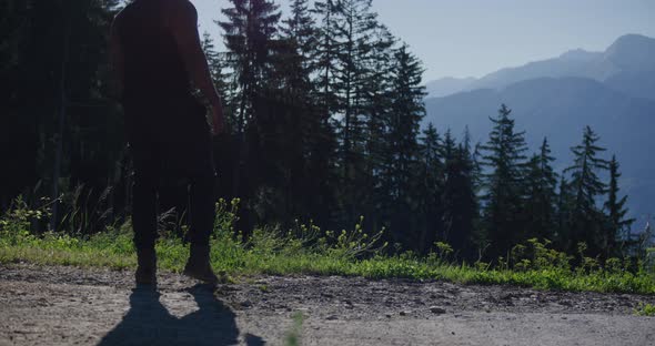 Black male traveler walking up to cliff ridge and looking out towards masssive mountain range in Swi