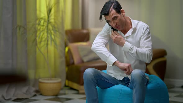 Wide Shot Portrait of Young Middle Eastern Positive Man Sitting on Bag Chair Talking on the Phone