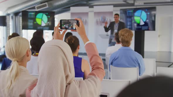 Woman in audience at a business conference filming with smartphone