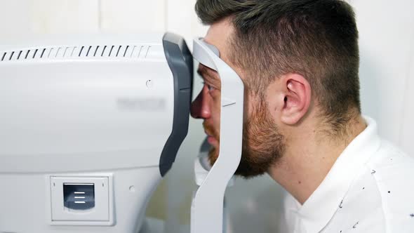 Male patient in ophthalmology clinic checks eyesight on special modern equipment.