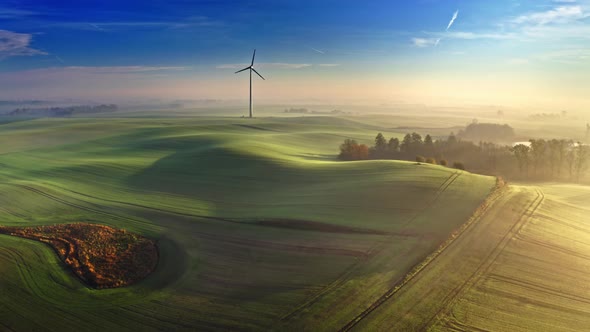 Stunning foggy sunrise on field with wind turbine