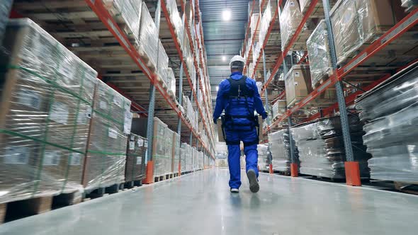 Worker in a Face Mask is Carrying a Box Through the Warehouse