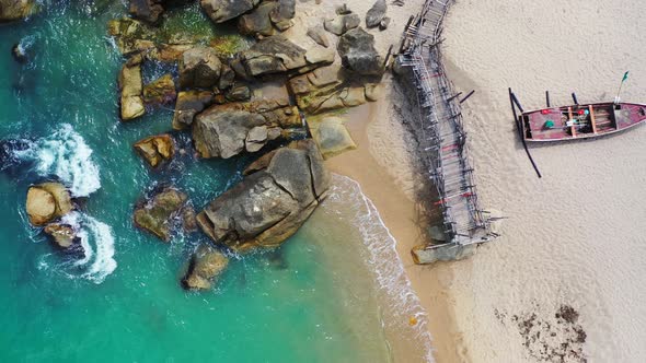 Sandy beach with rocks old wooden pier and turquoise seawater lapping on the sand. Aerial background