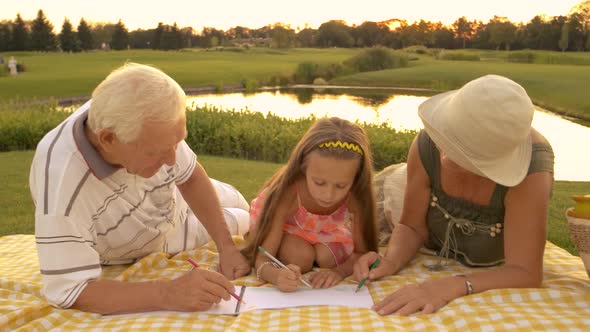 Grandparents Drawing with Granddaughter Outdoors.