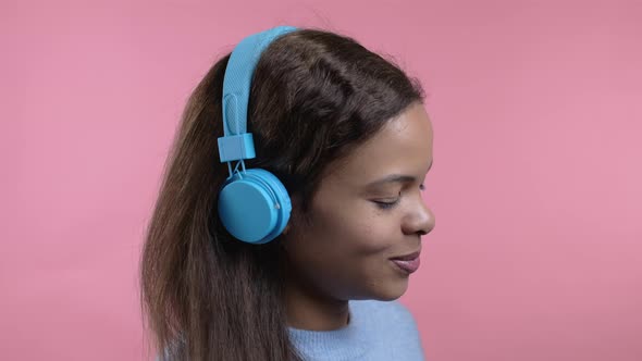 Mixed Race Woman Dancing with Wireless Blue Headphones Isolated on Pink Studio Background