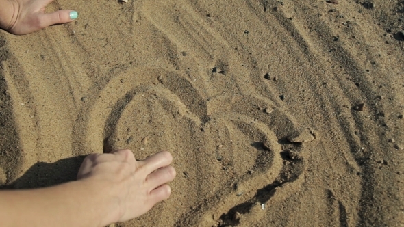 Girl Draws a Heart In The Hands Of The Sand