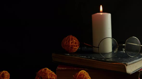 Burning Candle with Eyeglasses Standing on Old Books