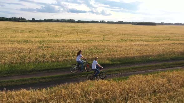 Girl with a Guy Riding a Bike Along a Wheat Field