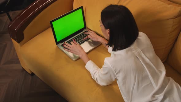 Young Woman Using Laptop with Green Screen Lying on the Couch Sofa at the Home