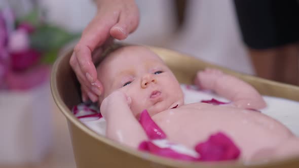 Charming Little Baby Girl Moving Hands and Legs Lying in White Milk Water with Mother Hands Putting