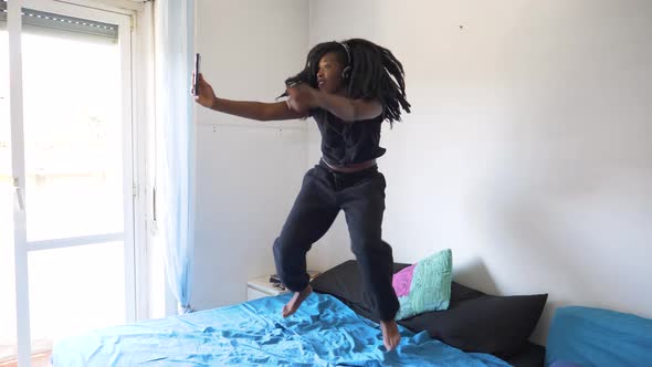 Slow motion shot of young woman dancing and using smartphone on bed