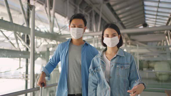 Portrait of Asian young passenger couple put wear face mask, standing in airport terminal.