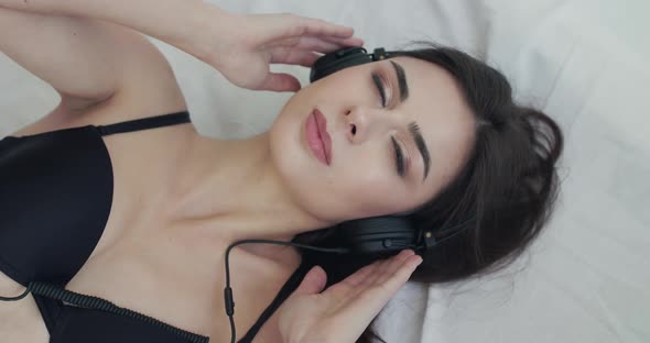 Woman on Bed Listens to Music on Headphones Opens Eyes and Smiles Into Camera