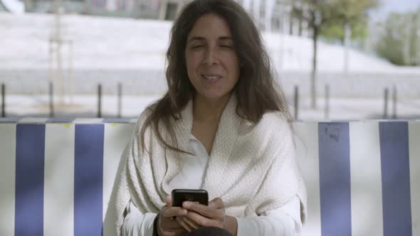 Smiling Middle Aged Brunette Holding Phone and Looking at Camera