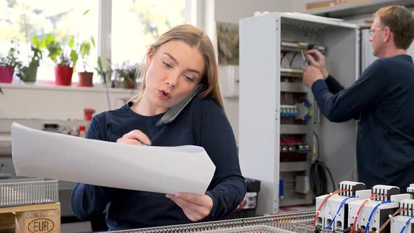 Female electrician having phone call while holding circuit plan