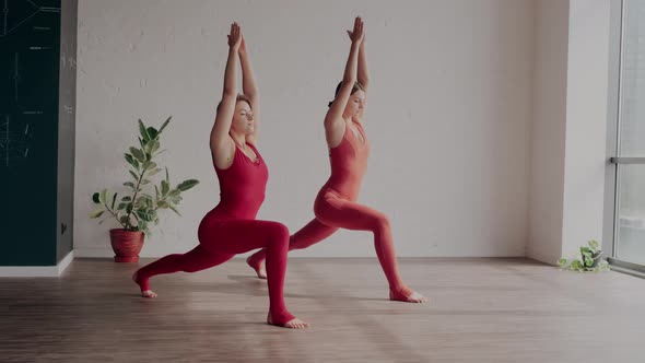 Two Women in Red Sports Uniforms Make Virabhadrasana in Yoga Studio