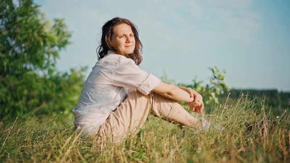 A Young Woman Sitting at the Dry Grass on the Hill and Enjoying the View