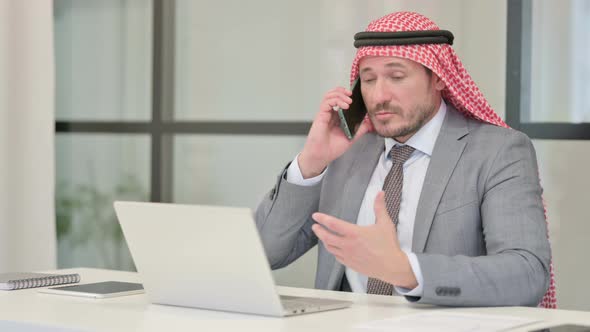 Middle Aged Arab Businessman Talking on Phone while using Laptop in Office