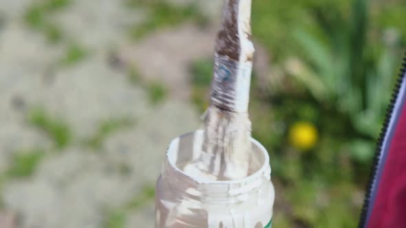 A Closeup of a Brush Dipped in a Glass Jar of White Paint
