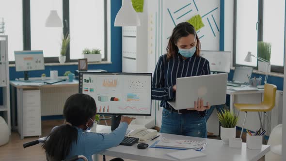 African Manager with Mask Working Checking Graphs Coworker Holding Laptop