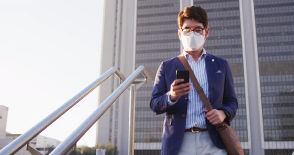 Asian man wearing face mask using smartphone while walking down the stairs at corporate park