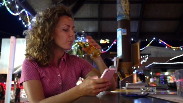 Woman Texting On Phone Drinking Beer In Bar