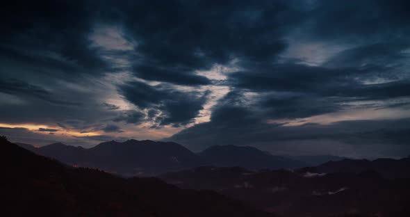 Sunset timelapse of moving clouds on sky with mountain landscape and city lights