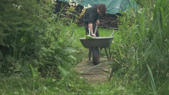 Young man out gardening filling wheelbarrow with clippings