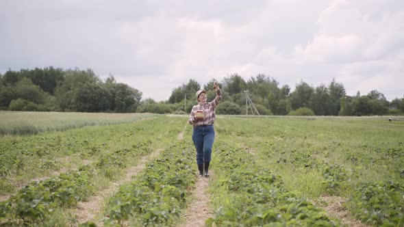 Happy Woman in Plaid Shirt Cap Cheerfully Walks Through Strawberry Field